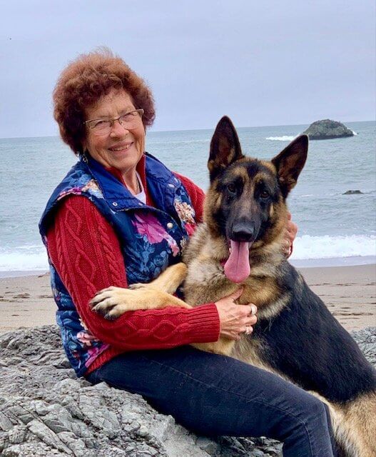 Gloria Birch sitting on a beach with her German Shepherd Dog