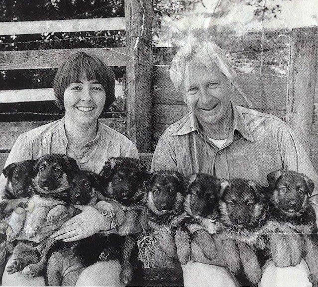 Black and white photo of a woman and man holding 8 German Shepherd Dog puppies