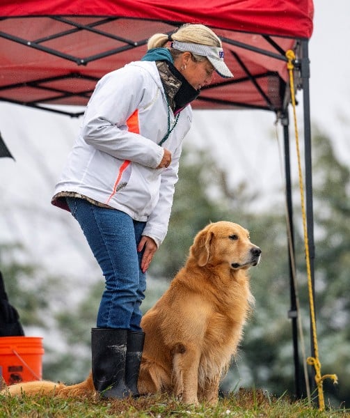 Woman with her Golden Retriever dog standing under a red tent at a field trial