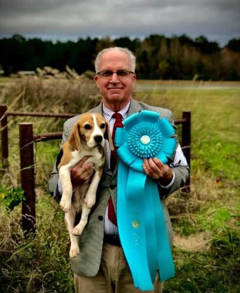 Owner Handler David Wolf standing in the field, holding a Beagle in one hand, and an accolade in the other