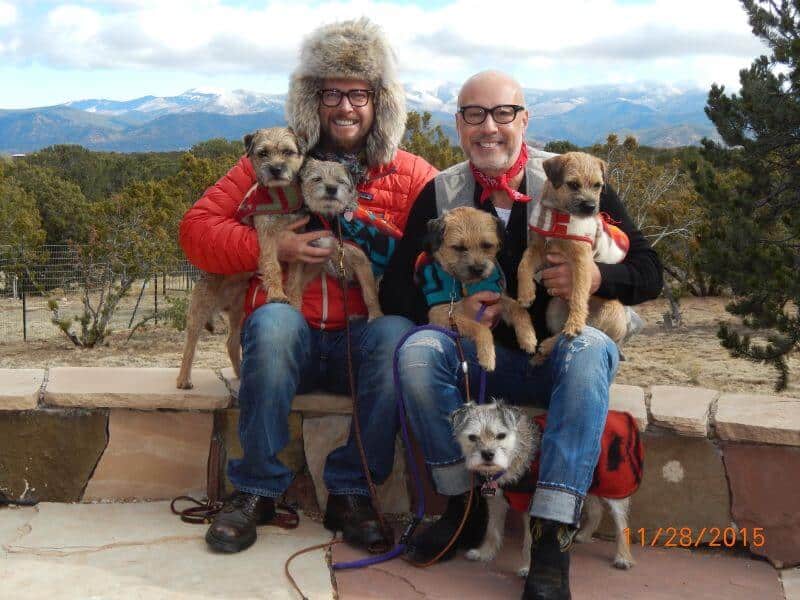 Peter Holson and companion sit on a bench with their dogs, enjoying the scenic backdrop of mountains.