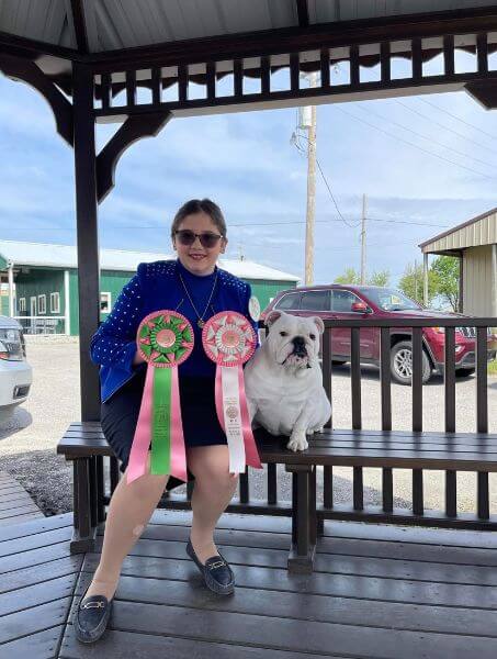 Zoe Brewer sits on a bench next to her Bulldog, showcasing her junior showmanship awards.