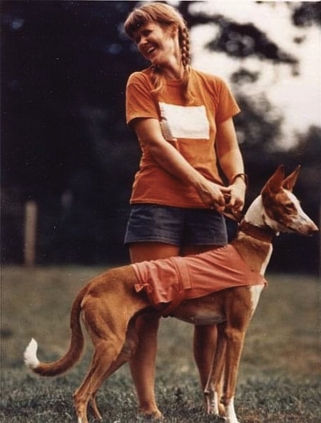 A woman in an orange shirt standing next to a dog.