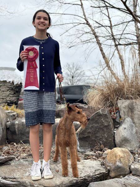 A girl holding an award and posing with a dog.