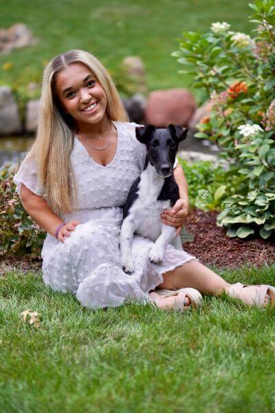 Annaliese North elegantly dressed in white holds a small dog in her arms.